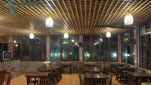 A restaurant with wooden tables and chairs, large windows, and hanging pendant lights. - Ninh Hoa Retreat (Tay Hoa Lu)