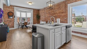 A modern kitchen with a brick wall, a large window, and a dining area with a table and chairs.