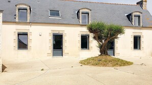 A two-story building with a symmetrical facade, multiple windows, and a central tree. - LARGE SEASIDE FARMHOUSE FOR 10 PEOPLE (Tréogat)