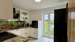 A modern kitchen with white cabinets, a black countertop, and a view of greenery through the sliding glass door.