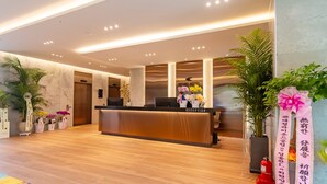 A hotel reception area with a wooden reception desk, potted plants, and a fire extinguisher. - HOUNDHOTELDAEGUHYUKSIN (Daegu)