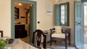 Un espace repas comprenant une table, des chaises et un banc. On peut apercevoir une cuisine à travers une porte ouverte.