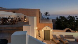 Une terrasse sur le toit comprenant un espace repas, des chaises longues et une porte donnant accès à un espace intérieur.