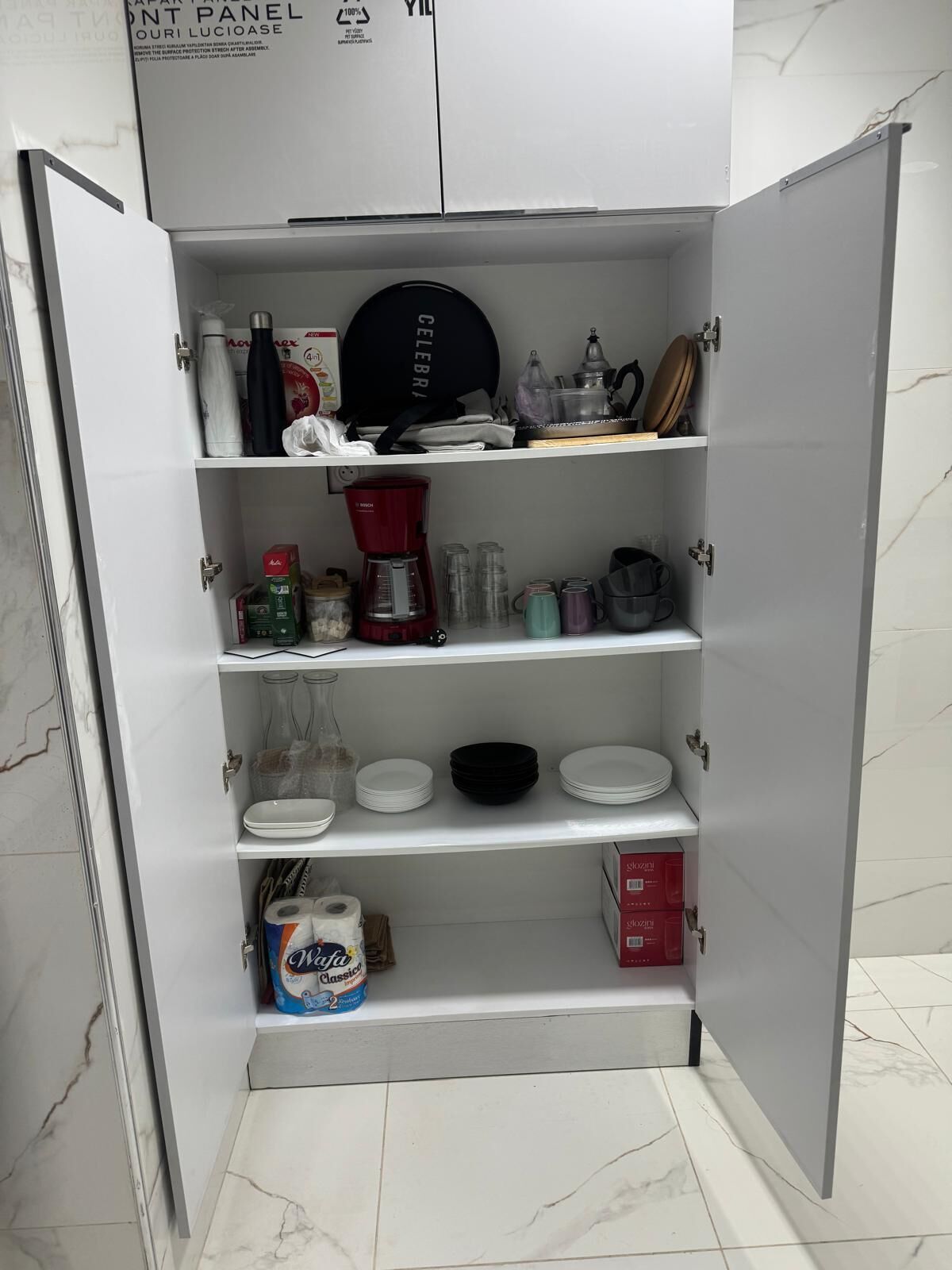 Un meuble de cuisine doté d’étagères contenant divers ustensiles et accessoires de cuisine, notamment une machine à café, des assiettes et des boîtes de rangement.