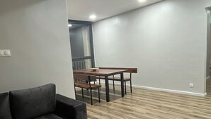 A modern living room with a sofa, a wooden coffee table, and a black ottoman. There is a dining table with chairs in the background.