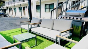 Un espace extérieur aménagé avec un canapé et des tables, un barbecue et un bâtiment en arrière-plan.