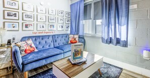 Una sala de estar con un sofá azul, una mesa de centro y cuadros enmarcados en la pared.