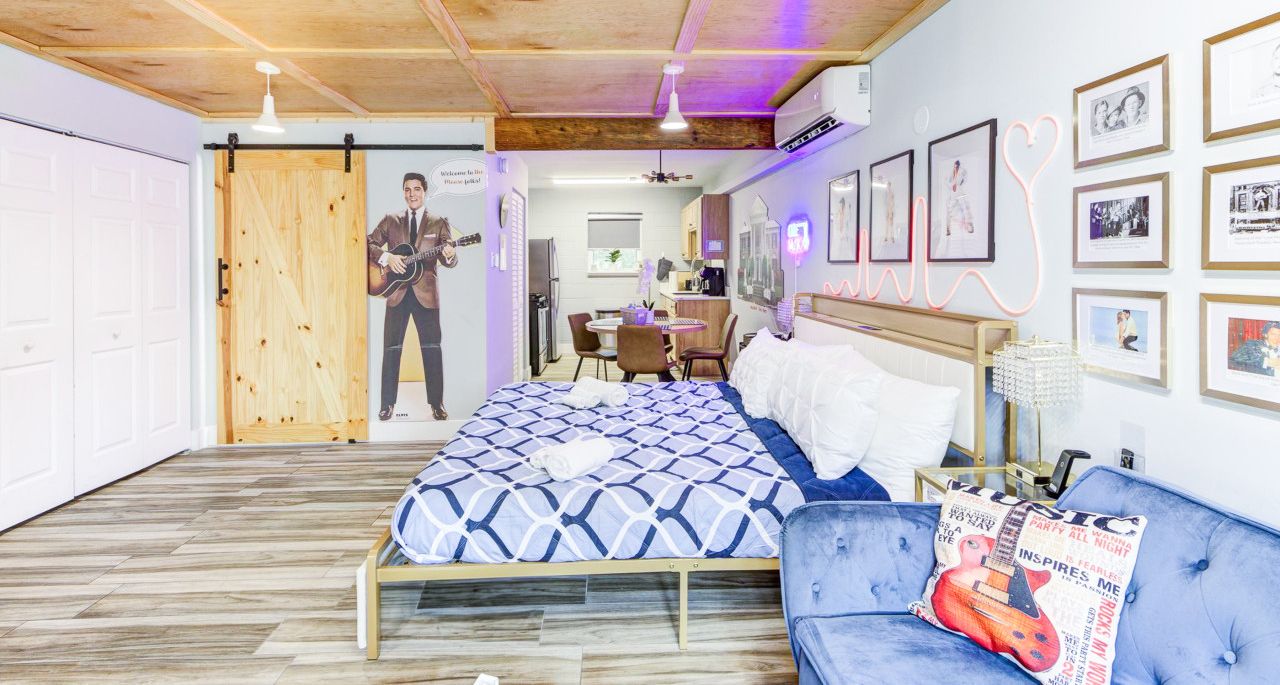 Un dormitorio con una cama, un sofá azul, una puerta de madera y cuadros en la pared.
