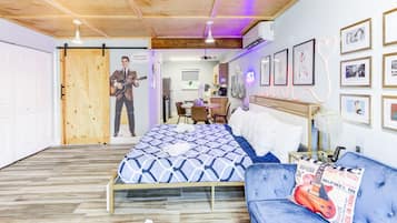 Un dormitorio con una cama, un sofá azul, una puerta de madera y cuadros en la pared.