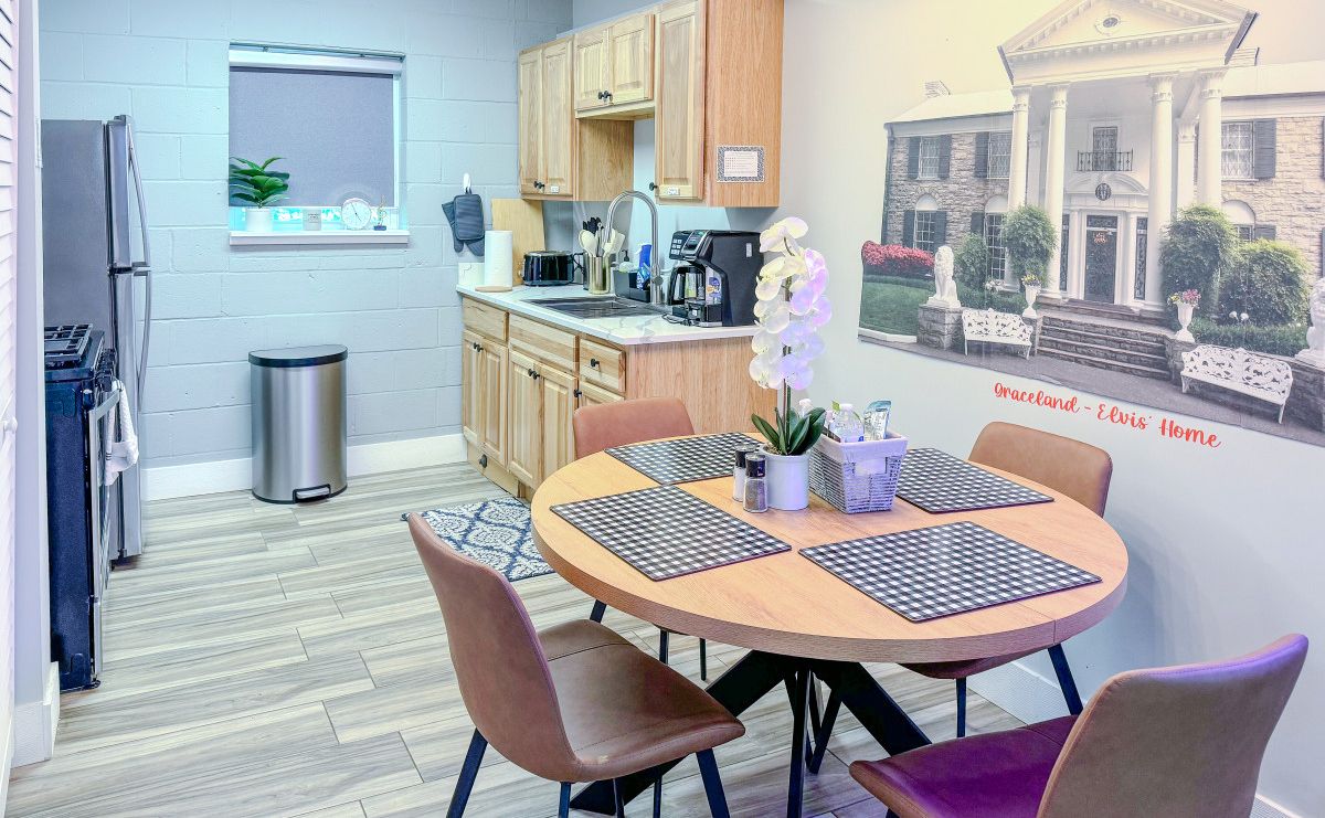A modern kitchen with wooden cabinets, a refrigerator, and a sink. There is a dining area with a round table and chairs.