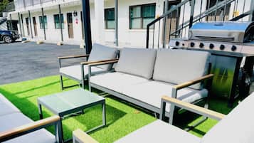 Un espacio al aire libre con sillones, mesas, una parrilla y un edificio al fondo.