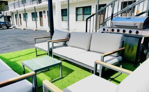 Un espace extérieur aménagé avec un canapé et des tables, un barbecue et un bâtiment en arrière-plan.