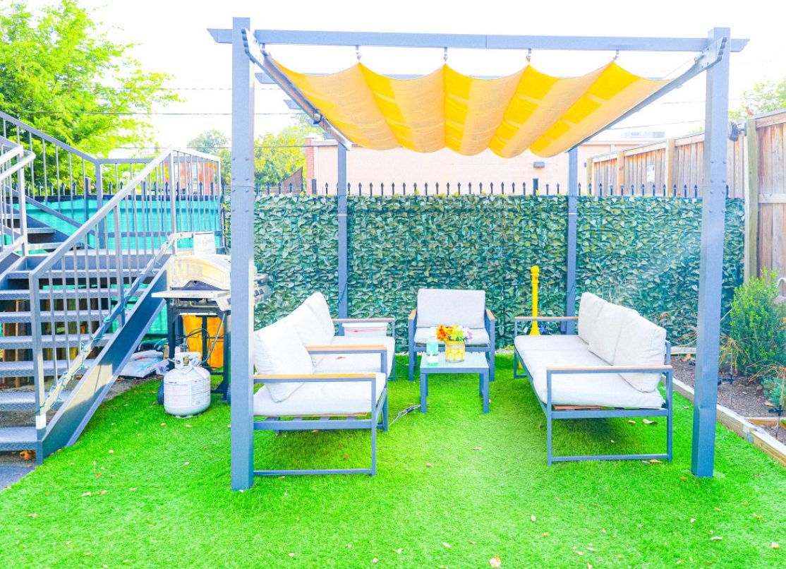 An outdoor patio with a pergola, two sofas, a coffee table, and a small table with a vase.
