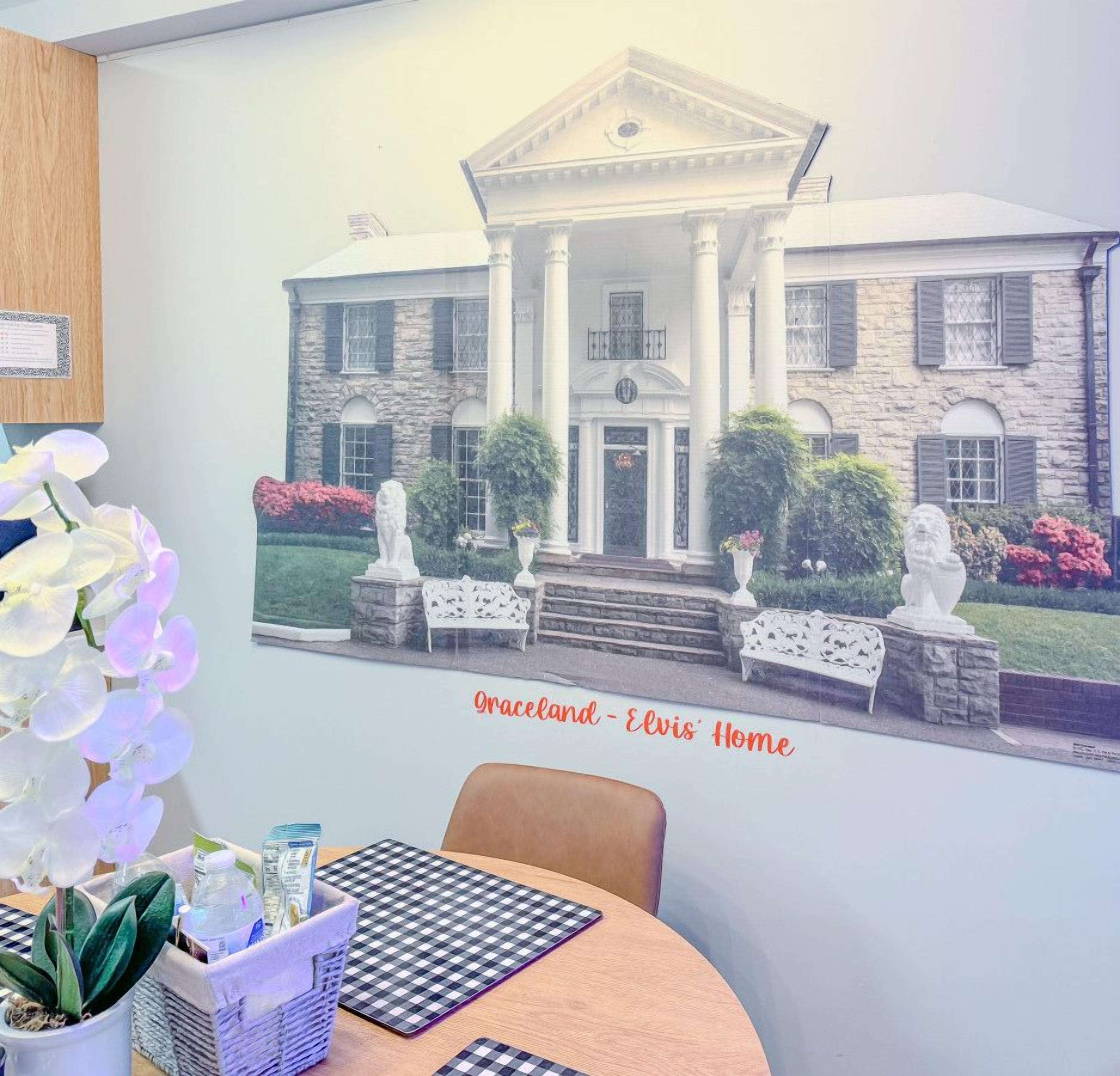 Una habitación con un cuadro enmarco de un edificio que dice 'Graceland - Casa de Elvis' y una mesa de comedor con sillas.