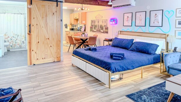 Une chambre avec un grand lit, un bureau et une chaise. Une porte coulissante donne accès à un coin cuisine.