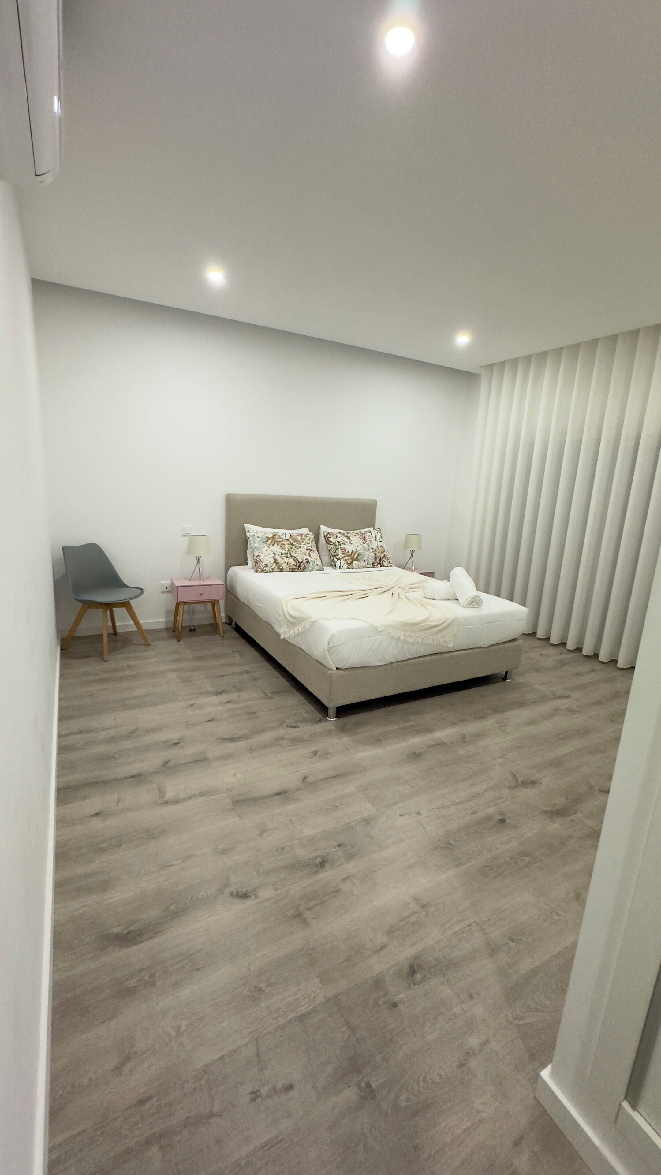 Un dormitorio moderno con una cama grande, una mesita de noche, una silla y una ventana con persianas.