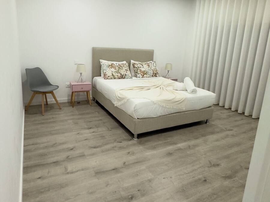 Un dormitorio moderno con una cama grande, una mesita de noche, una silla y una ventana con persianas.