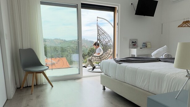 A modern bedroom with a bed, a chair, a TV, and a balcony with a view. - Vila Darte Alojamento Local (Vila de Rei)