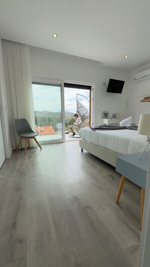 Un dormitorio moderno con cama, una silla, un televisor y un balcón con vistas.