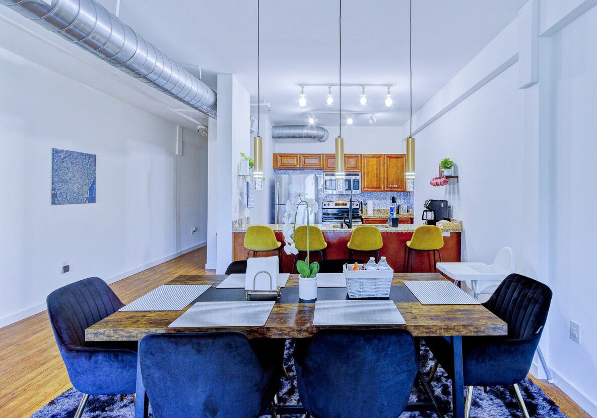 Un comedor moderno con una mesa de madera, sillas azules y una cocina al fondo.