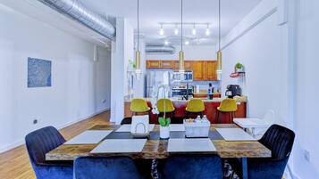 Un comedor moderno con una mesa de madera, sillas azules y una cocina al fondo.