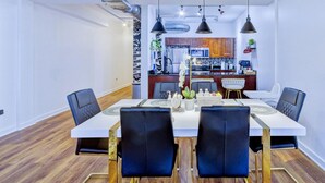 A modern dining area with a white table, black chairs, and pendant lights. A kitchen is visible in the background with wooden cabinets and a microwave. - BRAND NEW Modern Spacious Loft in Downtown with free parking (Memphis)