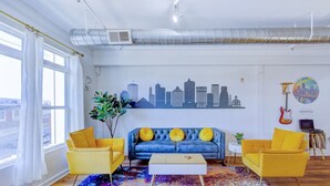 A modern living room with a blue sofa, yellow armchairs, a coffee table, and a city skyline mural on the wall. - BRAND NEW Modern Spacious Loft in Downtown with free parking (Memphis)