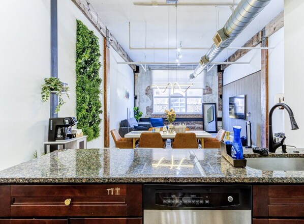 A kitchen with granite countertops, a dishwasher, a coffee machine, and a dining area with a table and chairs. - BRAND NEW Modern Spacious Loft in Downtown with free parking (Memphis)