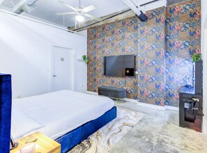 A bedroom with a bed, a TV mounted on the wall, a small bench, and a desk with a computer. - BRAND NEW Modern Spacious Loft in Downtown with free parking (Memphis)
