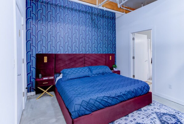 Camera da letto con una testiera rossa, una coperta a letto azzurra con motivo e una parete decorata.