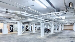 Un vaste espace de stationnement intérieur doté d’un sol en béton, de piliers structurels blancs et de tuyaux apparents au plafond.