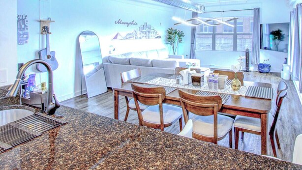 A modern kitchen with granite countertops, a dining area with wooden chairs, and pendant lighting.