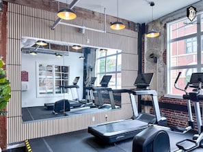 A gym with exercise equipment, a large mirror, and a brick wall.