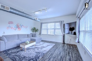 A modern living room with a grey sofa, a patterned rug, and a cityscape wall art.