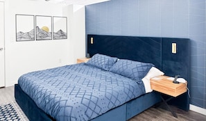 Ein Bett mit geometrischem Muster auf der Bettdecke, ein Nachttisch mit Lampe und eine Wand mit geometrischer Fliesenmusterung.