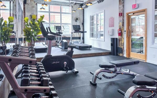 A gym with exercise equipment, large windows, and an exit sign.