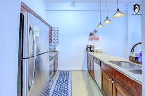 A kitchen with a stainless steel refrigerator, wooden cabinets, a patterned rug, and pendant lights.