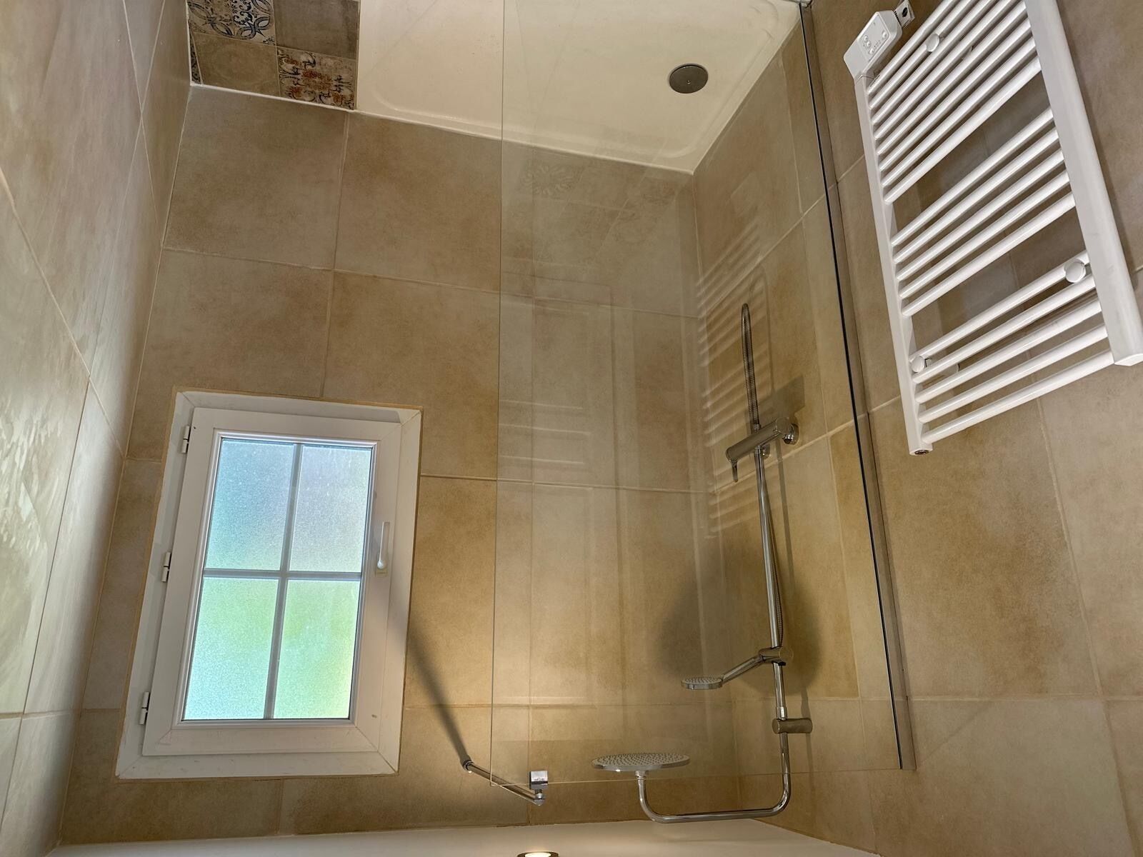 Une douche avec une porte en verre, une fenêtre et un porte-serviettes blanc.