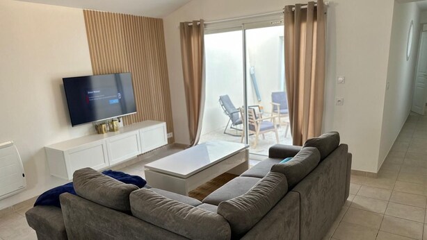 A modern living room with a grey sectional sofa, a flat-screen TV, a white coffee table, and a sliding glass door leading to a balcony. - Splendid house in a peaceful setting (Nieul-sur-Mer)