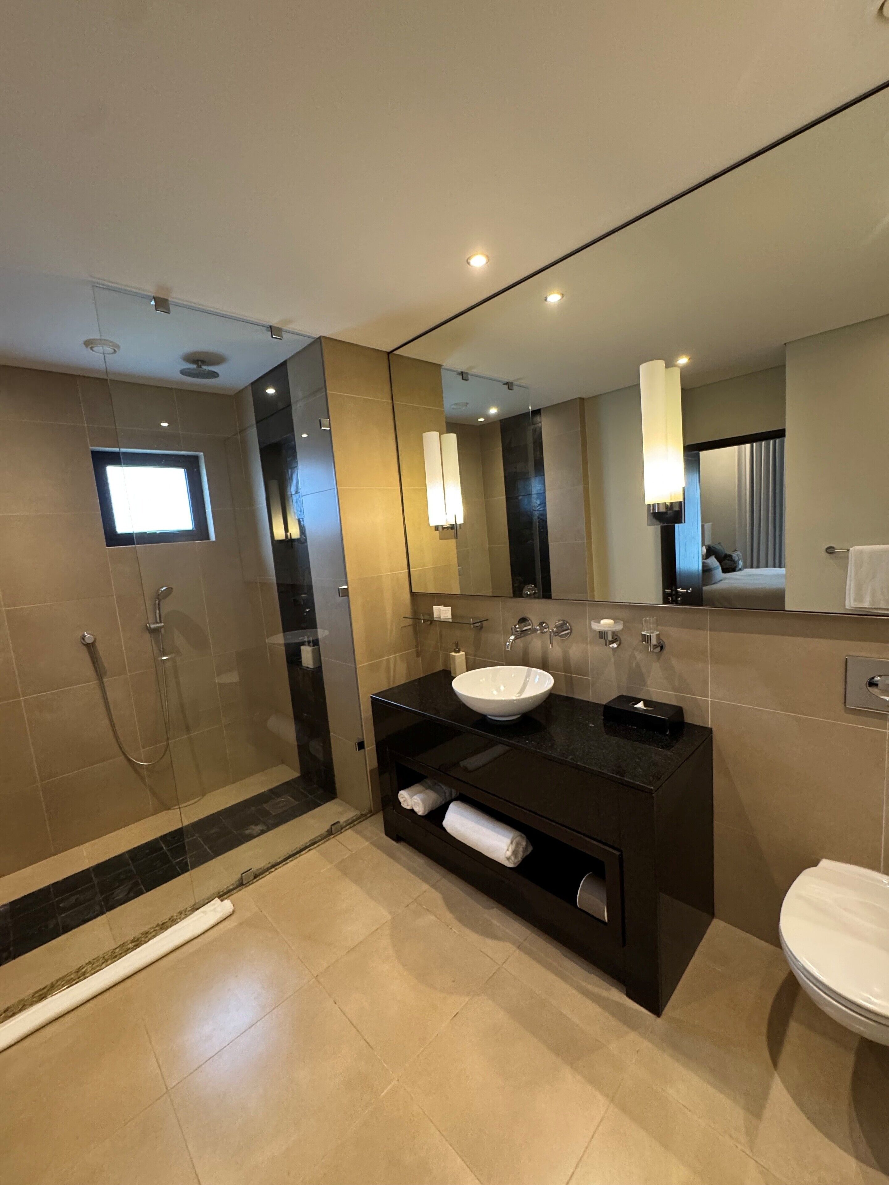 A modern bathroom with a glass-enclosed shower, a black vanity with a white sink, and a large mirror.