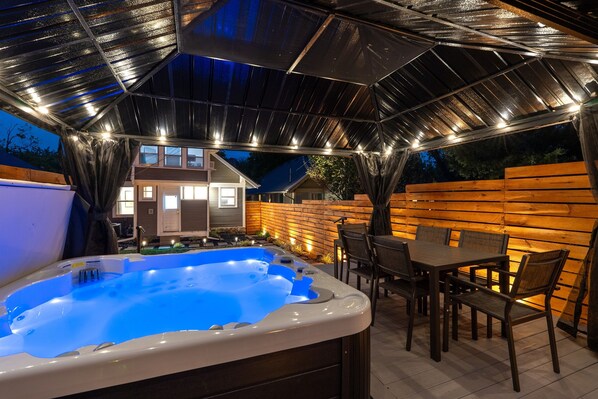 A hot tub under a covered patio with a table and chairs, surrounded by wooden fencing.