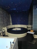 Una habitación con techo estrellado, una cama redonda, una bañera y una mesita con una caja.