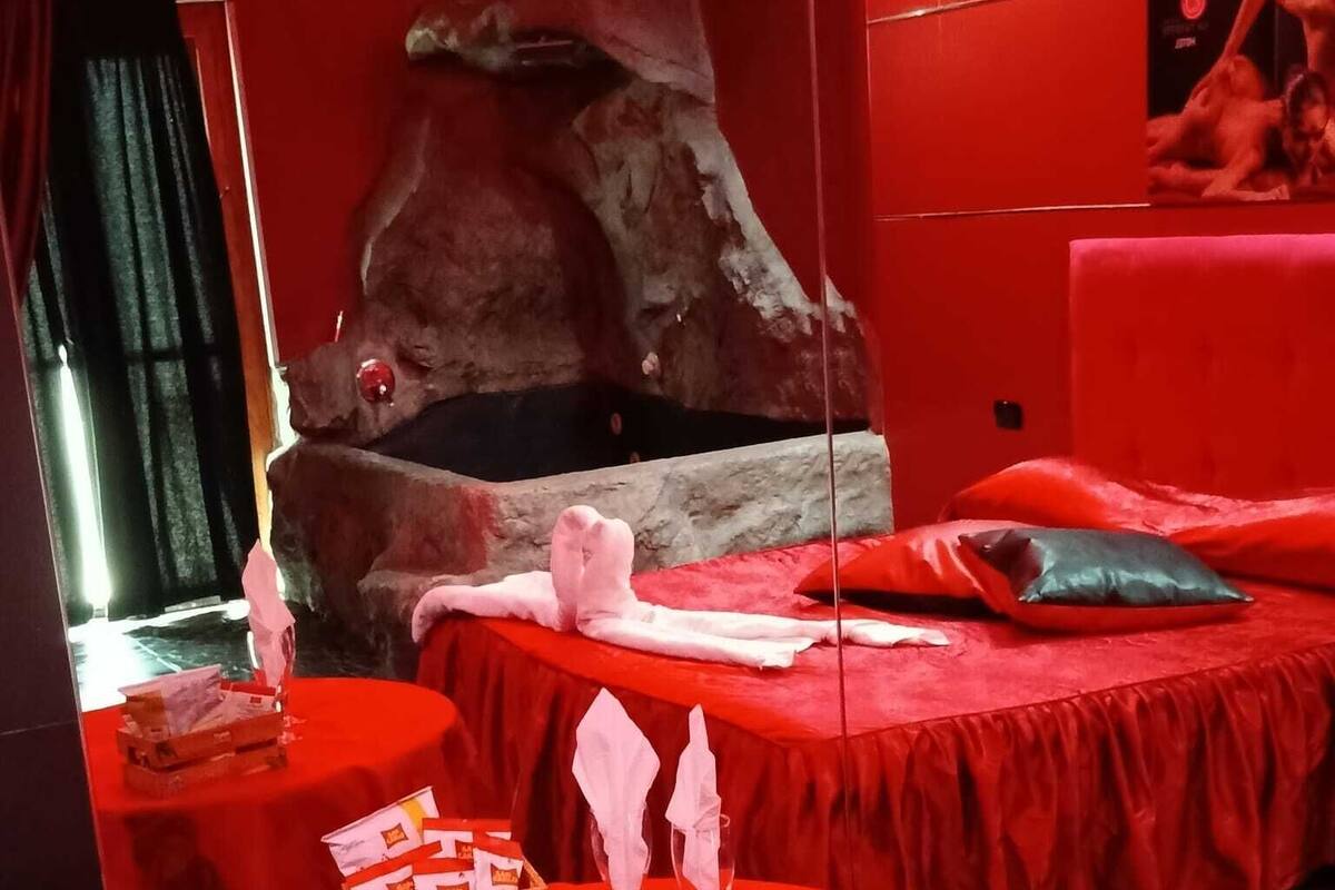 A room with red walls and a large rock feature. There are two beds with red bedding and pillows, and a table with a red tablecloth and some items on it.