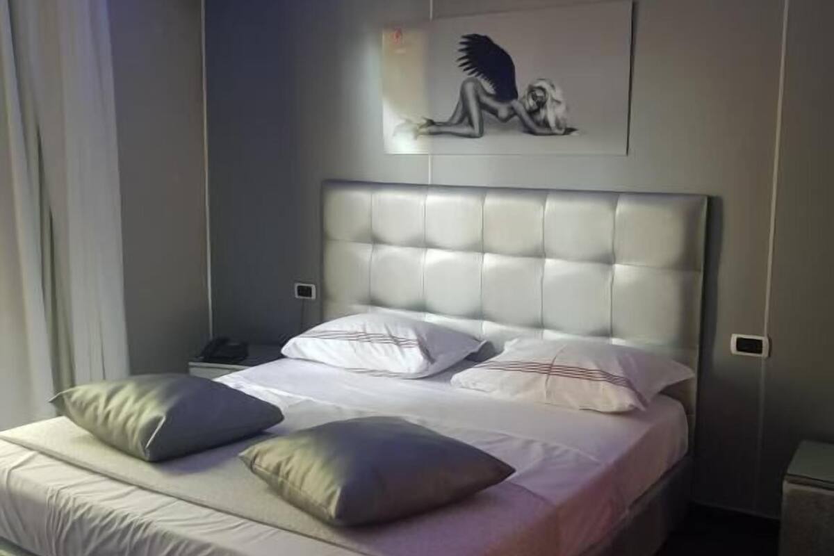A modern bedroom with a large bed, a headboard, and a wall-mounted artwork of a winged figure.