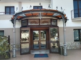 Entrada de hotel con un arco decorativo, puertas de cristal y una pared de piedra.