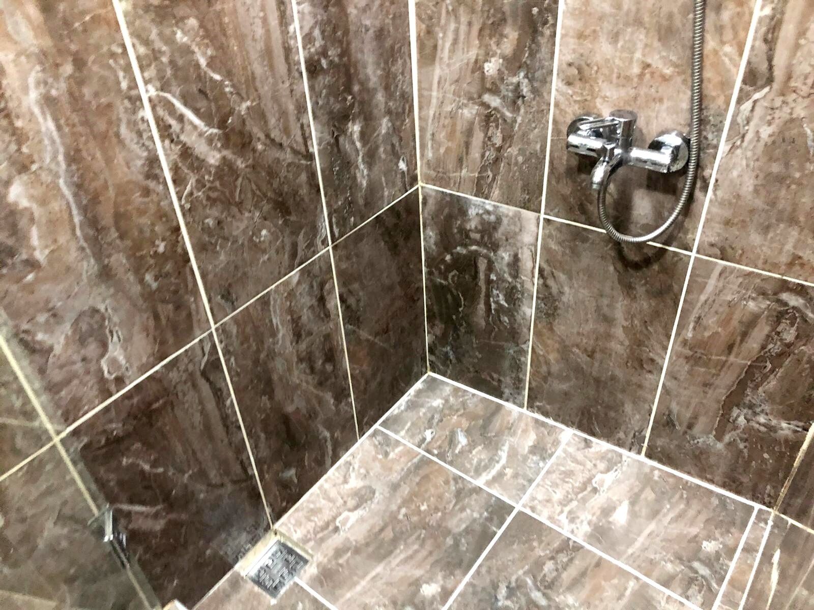 A bathroom with marble tiles, a shower area, and a visible drain.