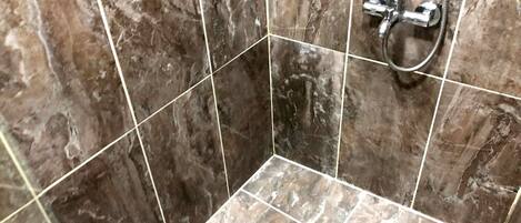 A bathroom with marble tiles, a shower area, and a visible drain.