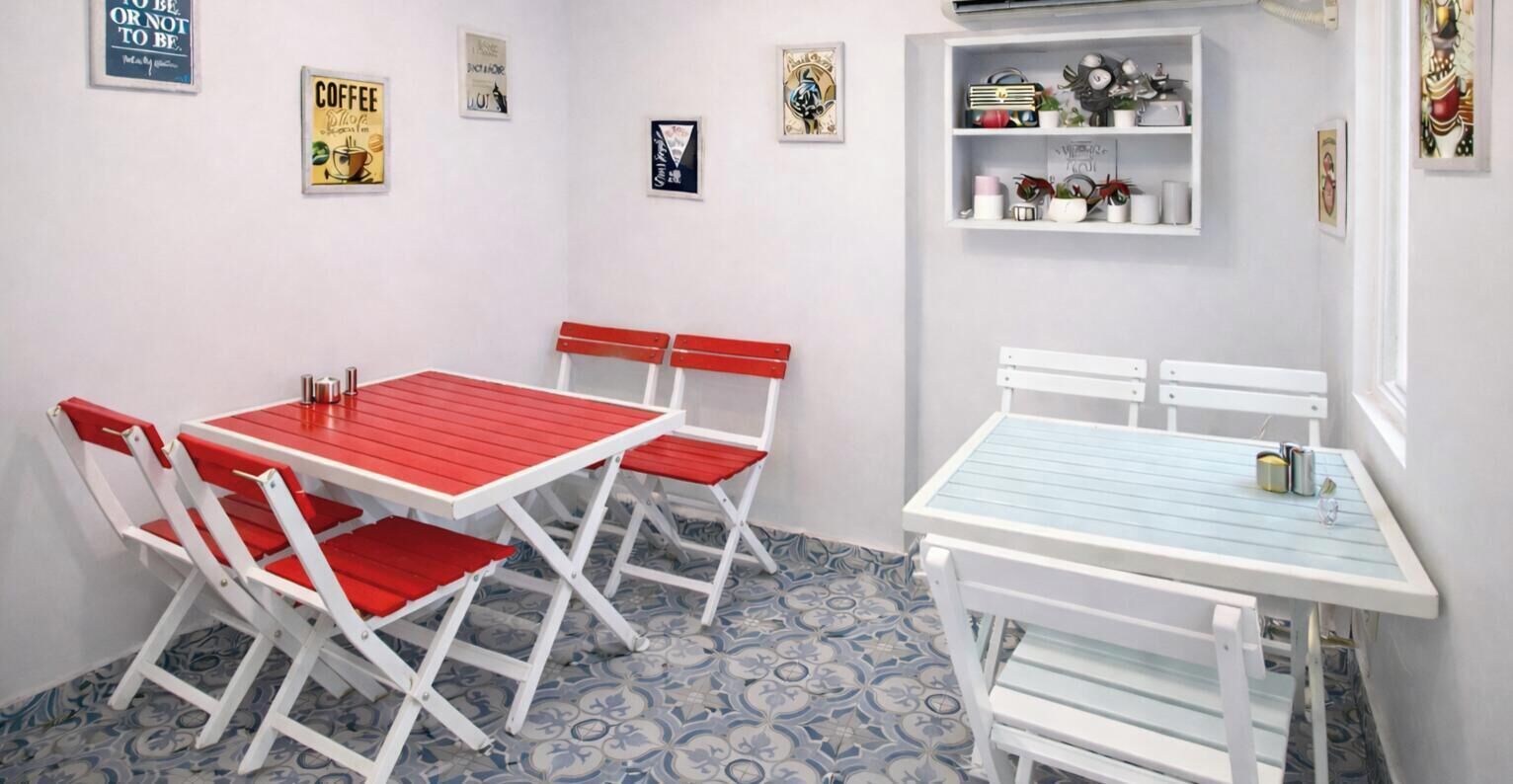 A room with a red and white table and chairs, a blue and white patterned floor, and a shelf with various items.