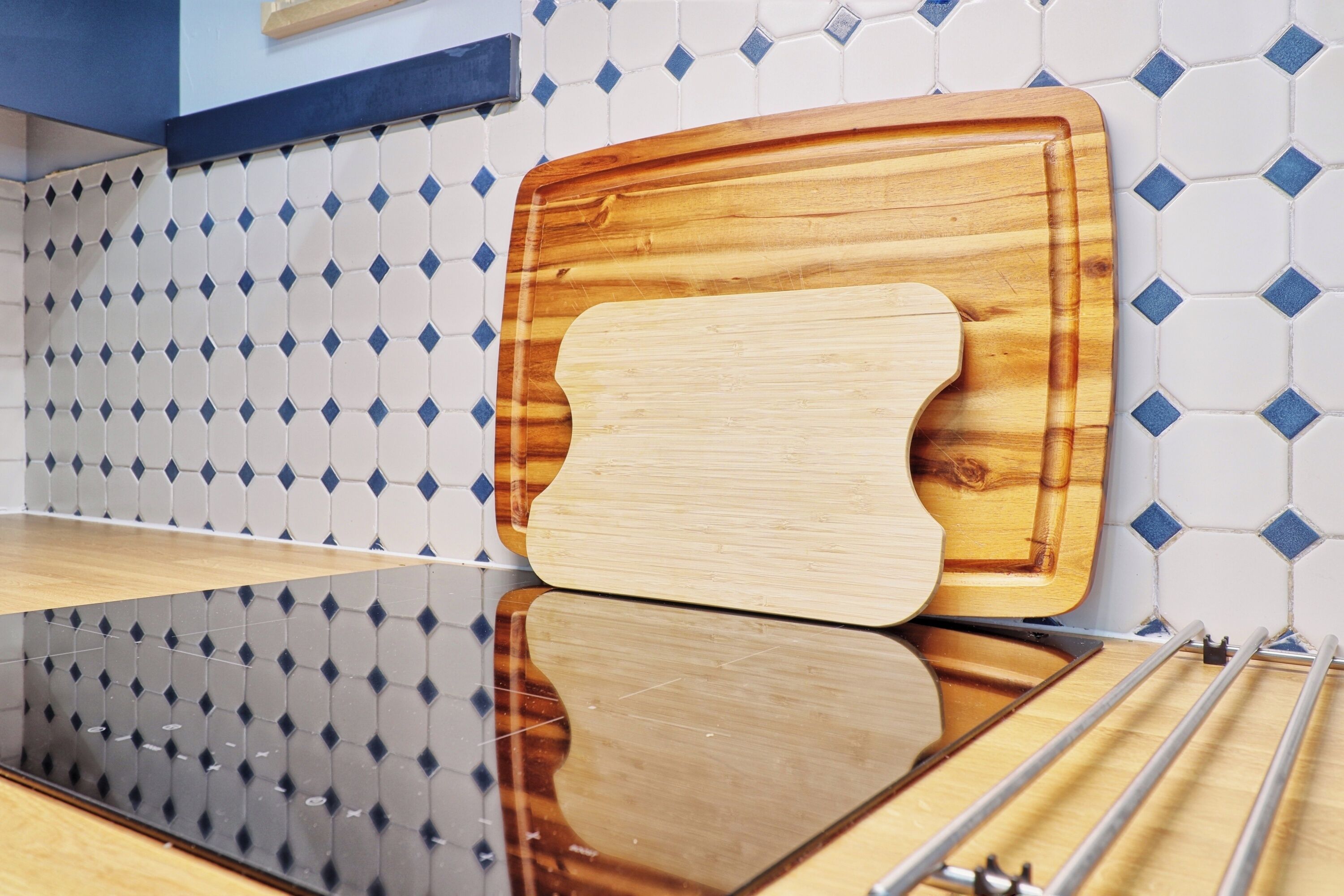 A kitchen with a wooden cutting board on a reflective countertop, a tiled backsplash, and a metal rack.