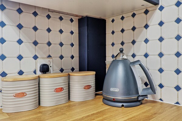 A kitchen area with a DeLonghi electric kettle, three containers labeled 'SUGAR' and 'TEA', and a power outlet.